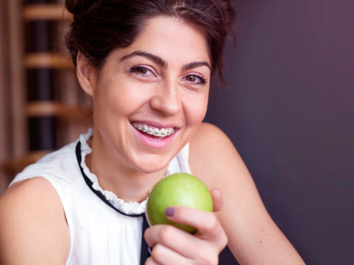 Mujer con brackets sonriendo mientras se come una manzana verde